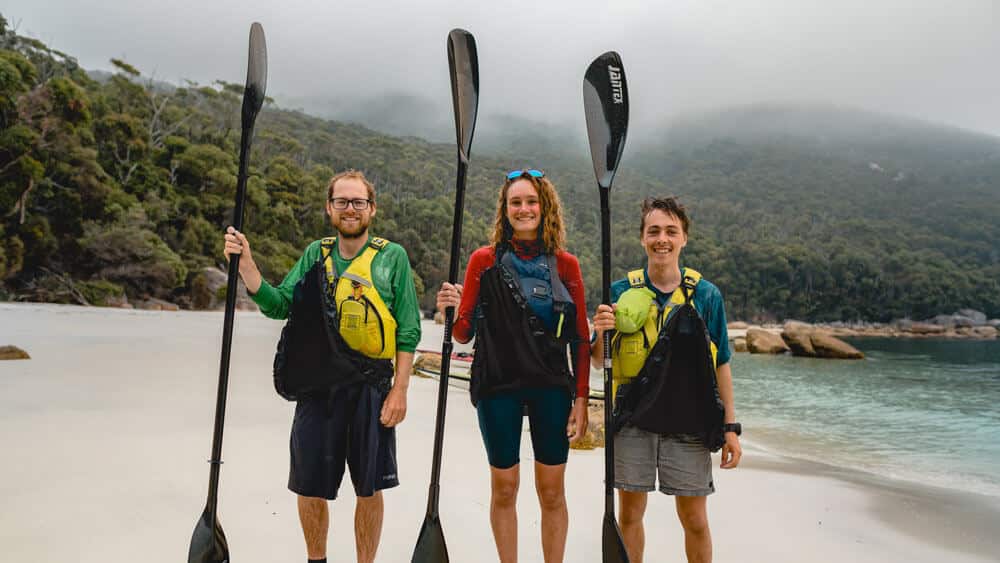 the team on a beach holding their kayak paddles