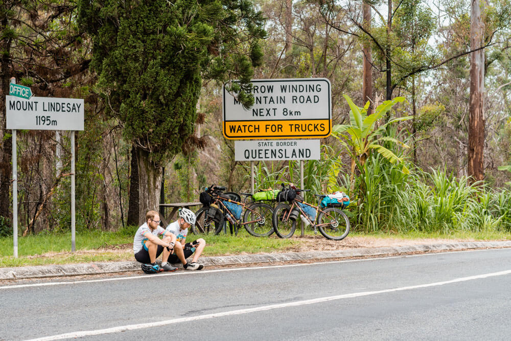 cyclists sat on the curb at the Queensland border
