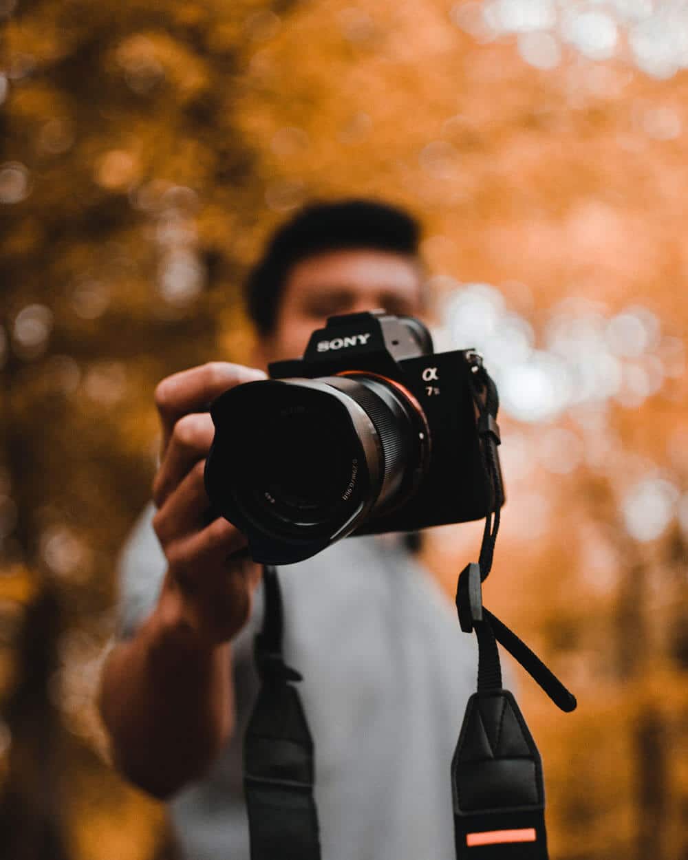 out of focus orange autumnal background, guy holding camera towards the lens covering his face