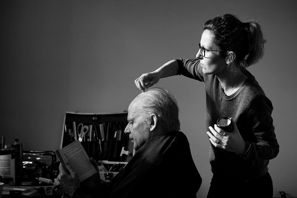 male actor reading his lines while having his hair combed by a woman